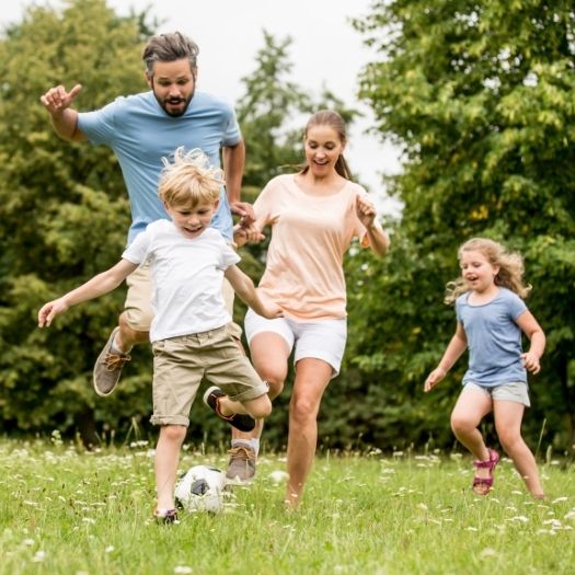 A family runs and plays soccer together in a sunny park, showing active outdoor living supported by well‑managed asthma care.