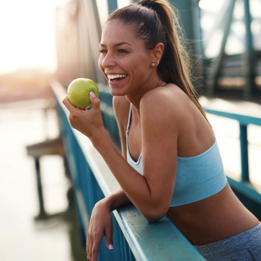 A woman in athletic wear leans on a railing while holding a green apple, reflecting healthy habits that support strong immune function.