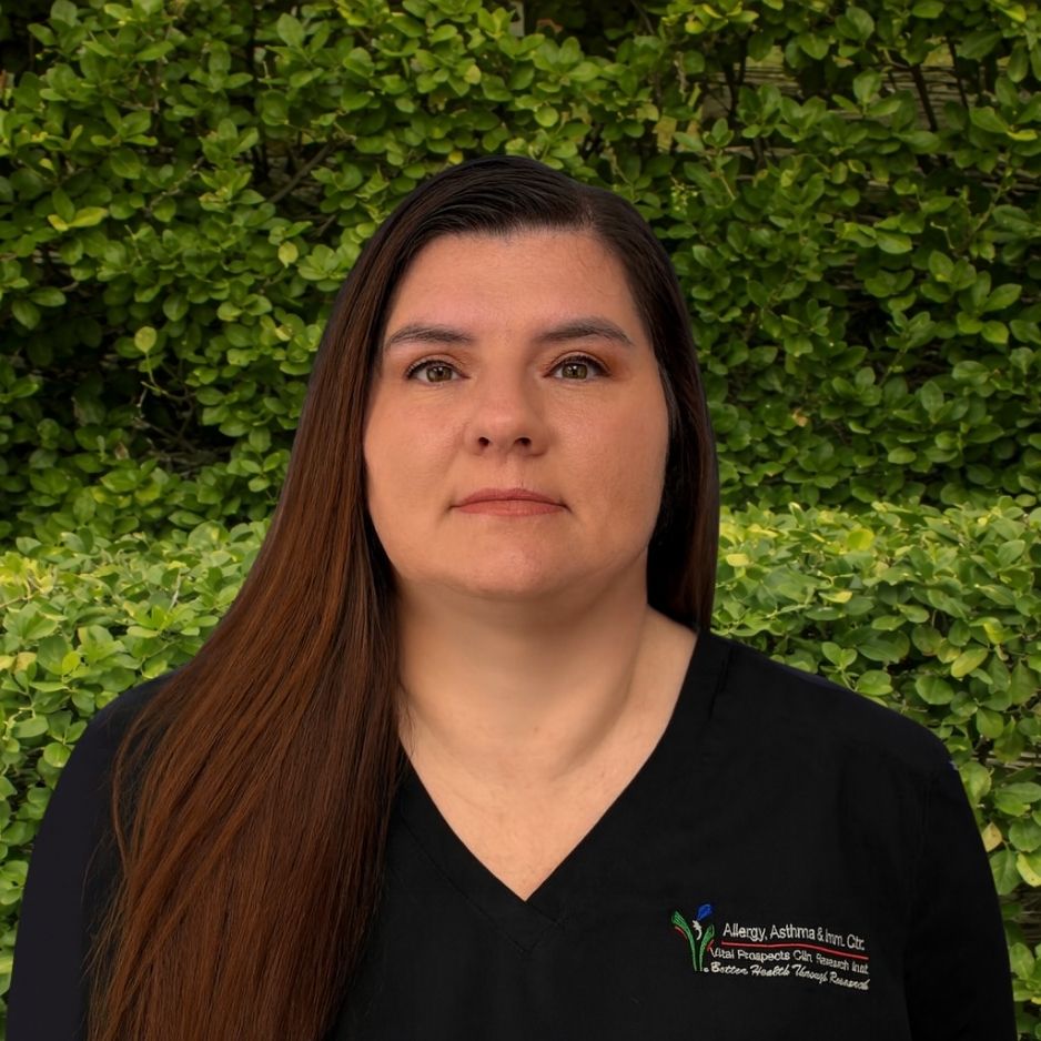 A member of the research team in black scrubs stands in front of green bushes, representing dedication for research and healing patients.