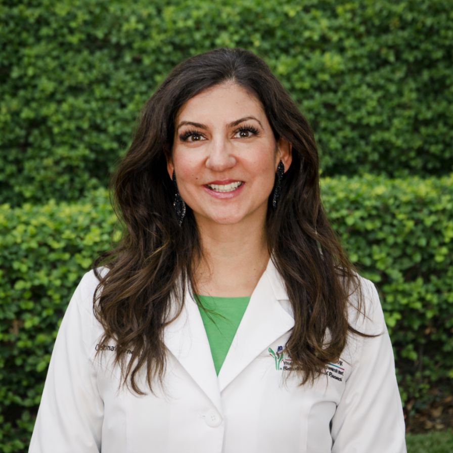A healthcare professional in a white lab coat stands outdoors against green foliage, representing advanced nursing expertise in allergy and immunology care.