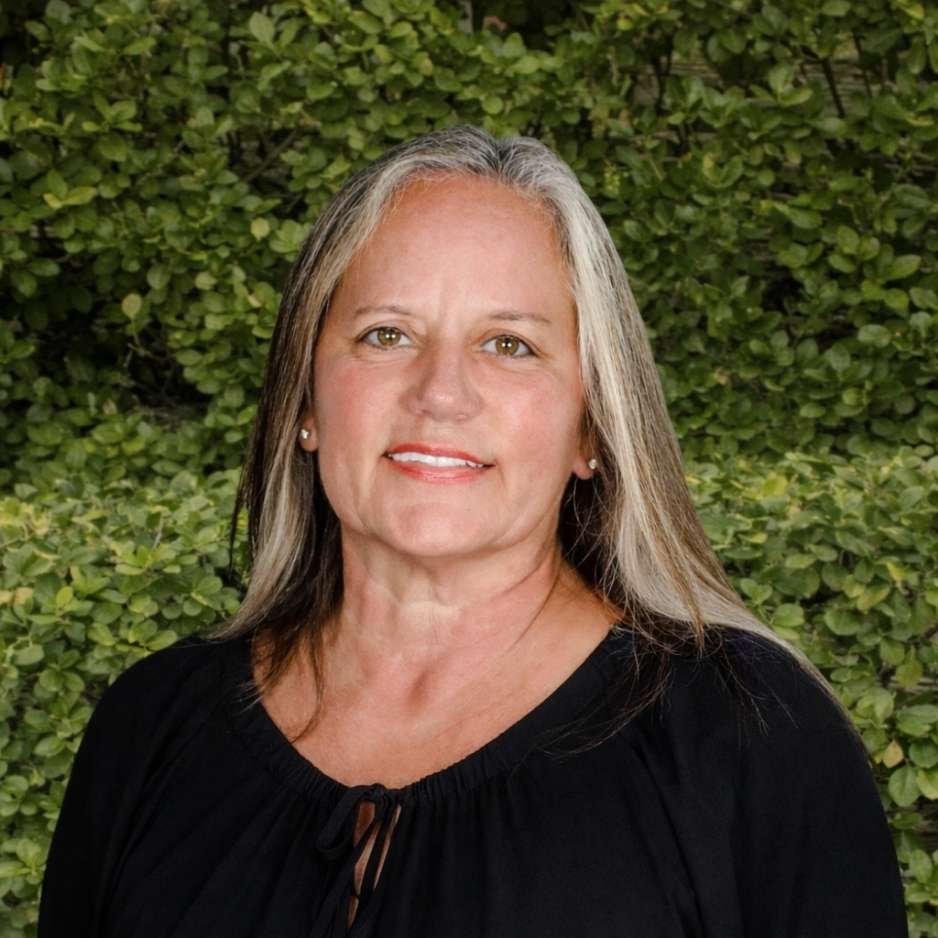 A staff member in a black blouse stands before green foliage, representing welcoming patient support within the allergy and asthma clinic.