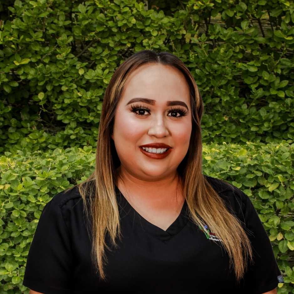 A clinical staff member in black scrubs stands in front of green shrubs, representing hands‑on support for allergy and asthma patients.
